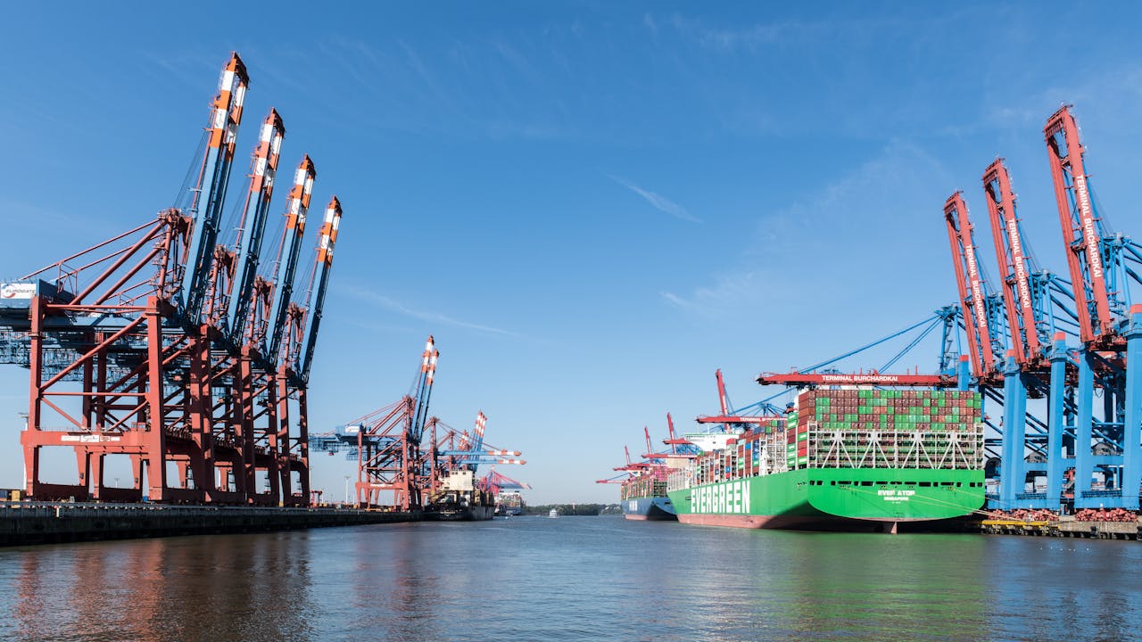 about-img View of container ships and cranes at the busy Port of Hamburg under a clear sky.